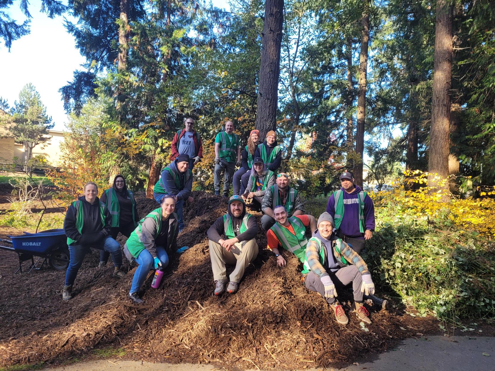 Group of REI workers gathered atop a pile of tree mulch after a successful work party