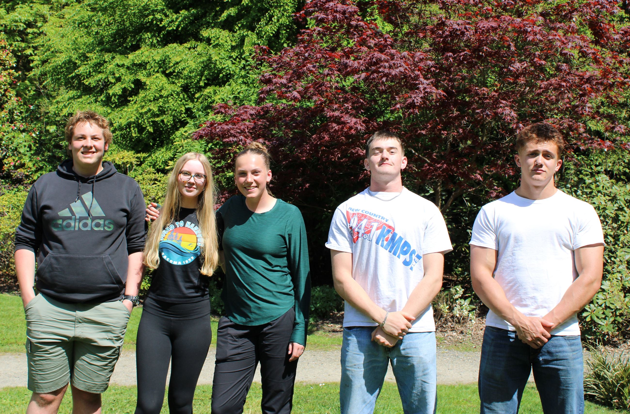 A group of five highschool students stand together in front of trees